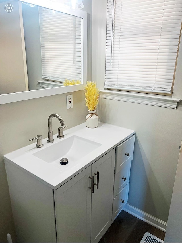 bathroom with visible vents, vanity, baseboards, and wood finished floors