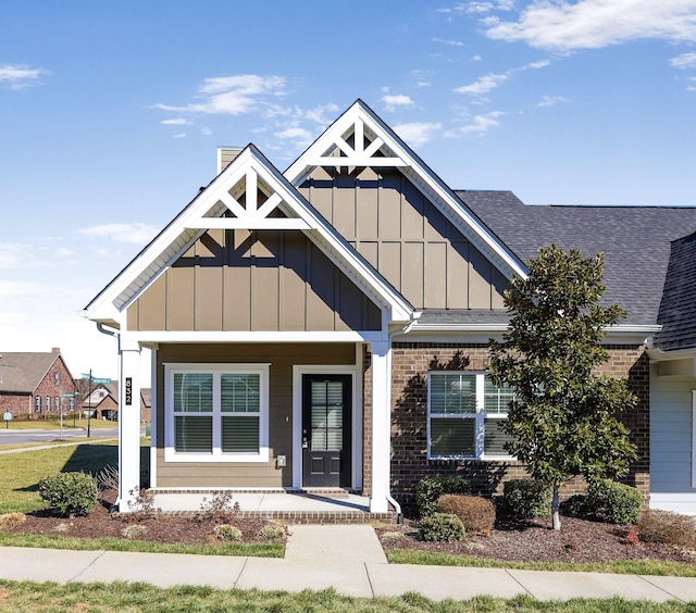 view of front facade with board and batten siding, brick siding, and roof with shingles