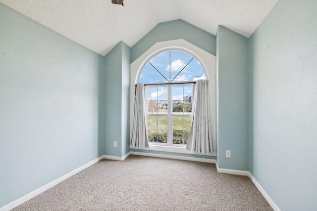 carpeted spare room featuring baseboards and vaulted ceiling