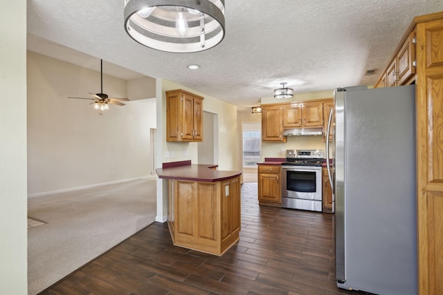 kitchen with dark countertops, appliances with stainless steel finishes, brown cabinetry, open floor plan, and dark wood-type flooring