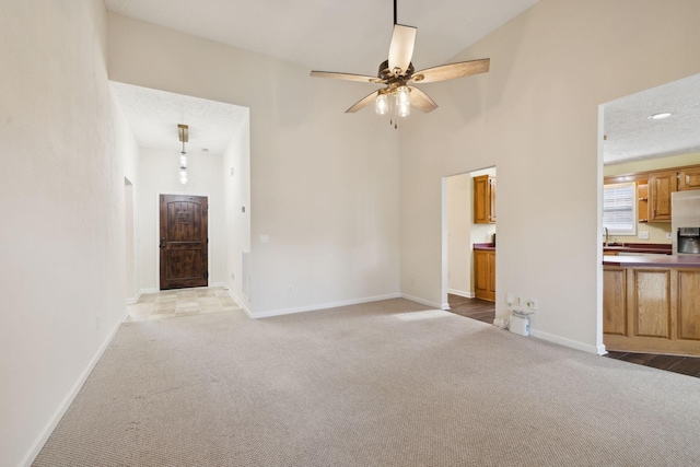 unfurnished living room with ceiling fan, light colored carpet, a sink, a towering ceiling, and baseboards