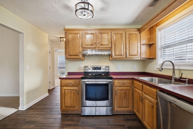 kitchen with wood finish floors, range hood, stainless steel appliances, dark countertops, and a sink