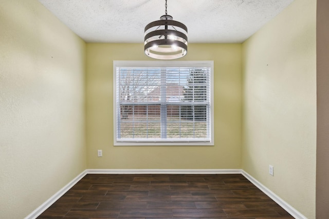 unfurnished dining area featuring dark wood-style floors, a textured ceiling, a notable chandelier, and baseboards