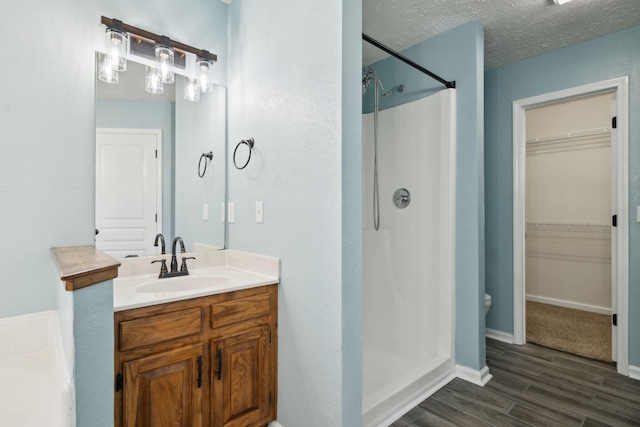 bathroom featuring a walk in closet, a stall shower, a textured ceiling, vanity, and wood finished floors