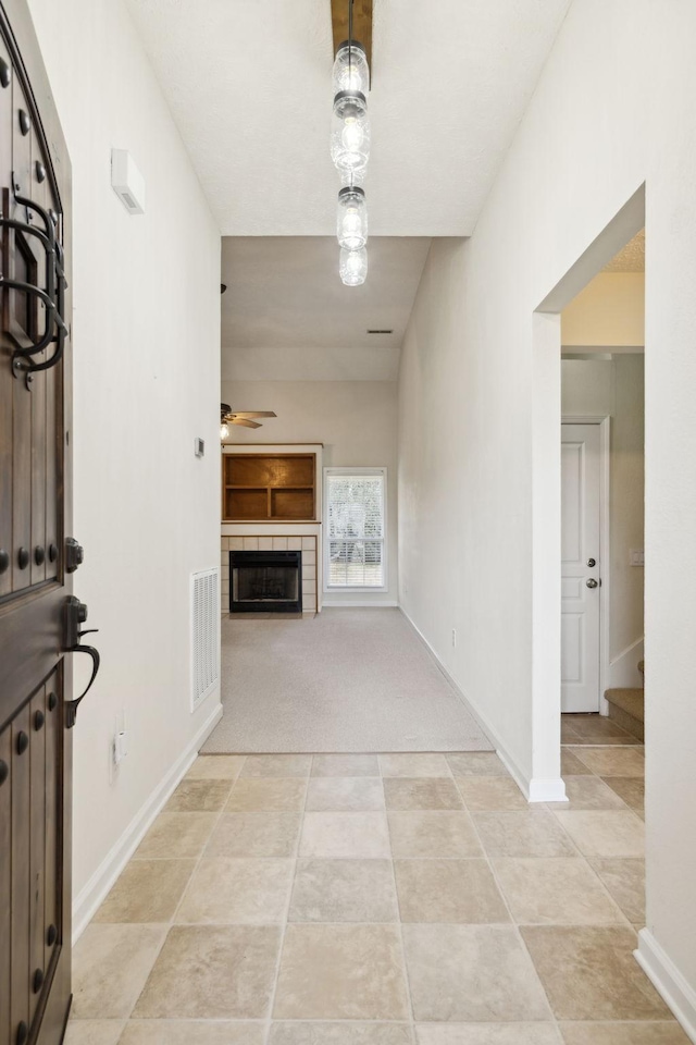 unfurnished living room featuring baseboards, visible vents, a ceiling fan, and a tiled fireplace