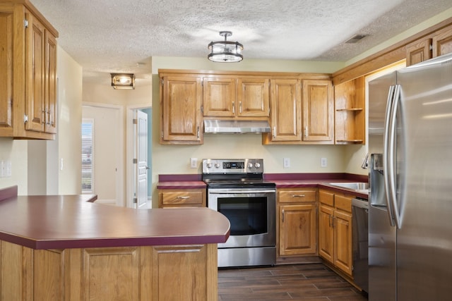 kitchen featuring a peninsula, under cabinet range hood, dark countertops, and appliances with stainless steel finishes