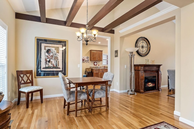 dining space with beam ceiling, light wood-style flooring, an inviting chandelier, a glass covered fireplace, and baseboards