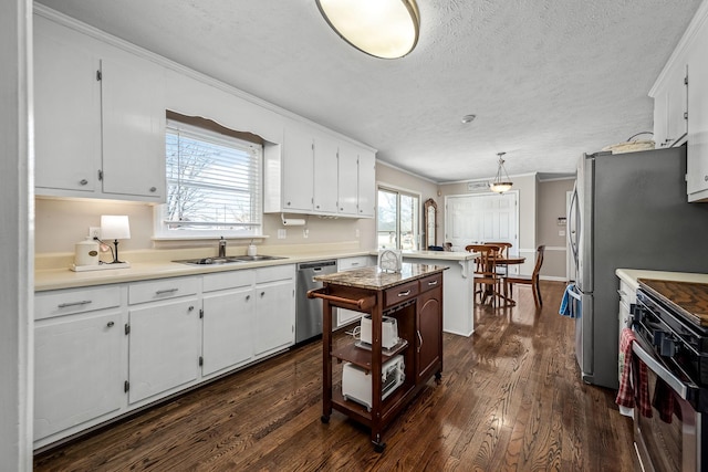 kitchen with stainless steel appliances, light countertops, white cabinetry, pendant lighting, and a sink