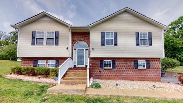 raised ranch with a front yard and brick siding