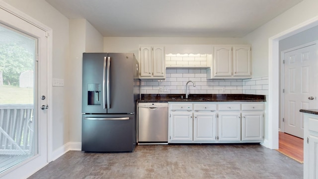 kitchen featuring stainless steel appliances, dark countertops, tasteful backsplash, white cabinets, and a sink
