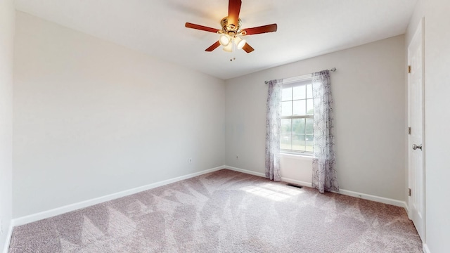 spare room featuring light colored carpet, ceiling fan, visible vents, and baseboards