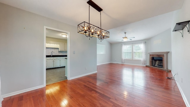 unfurnished living room with a sink, a fireplace, wood finished floors, and baseboards