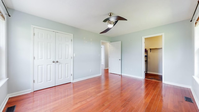 unfurnished bedroom with a closet, wood finished floors, visible vents, and baseboards