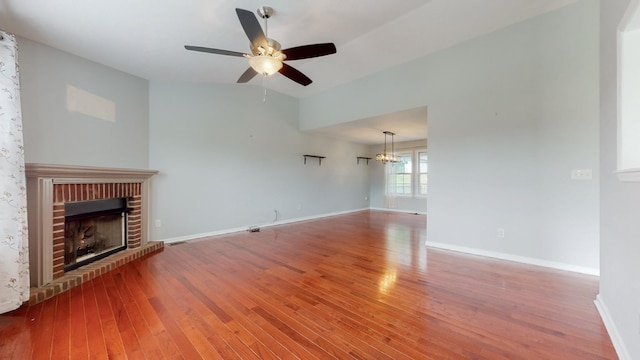 unfurnished living room featuring ceiling fan with notable chandelier, wood finished floors, visible vents, baseboards, and a brick fireplace