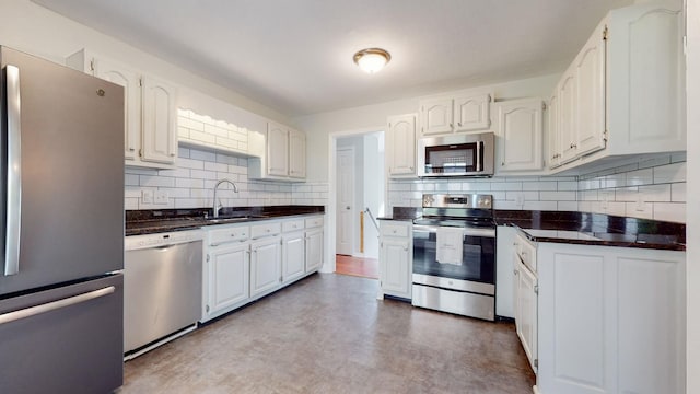 kitchen with appliances with stainless steel finishes, dark countertops, white cabinets, and a sink