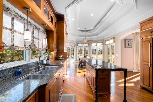 kitchen featuring pendant lighting, brown cabinets, a raised ceiling, a sink, and dark stone countertops