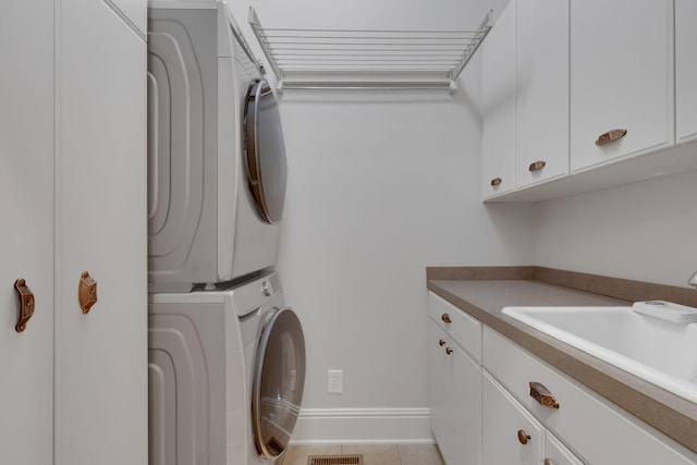 clothes washing area with cabinet space, visible vents, stacked washing maching and dryer, a sink, and light tile patterned flooring