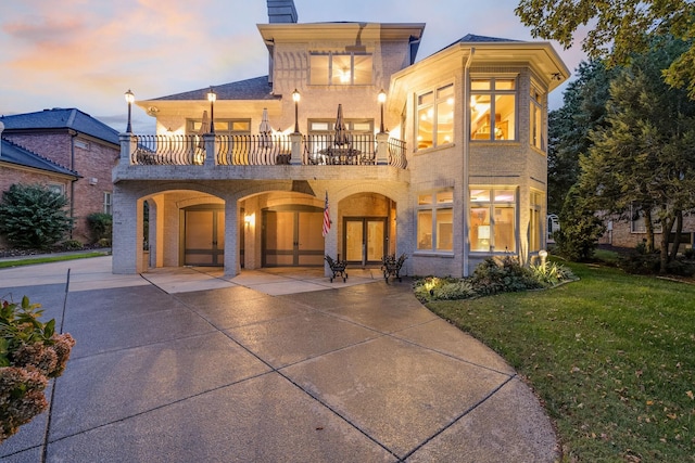 view of front facade with a balcony, a garage, brick siding, driveway, and a front lawn