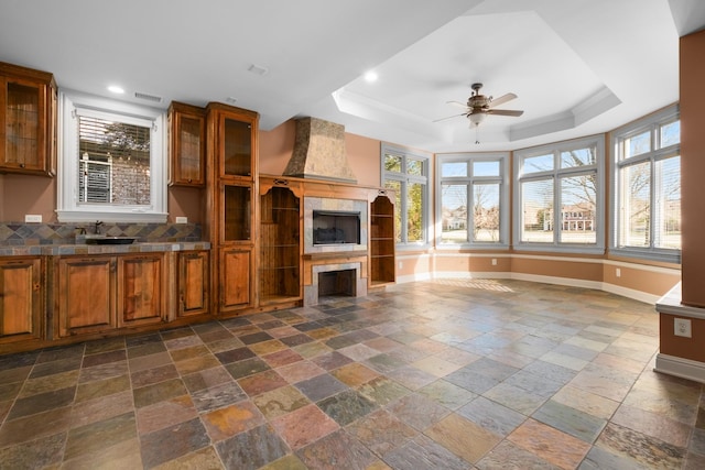 unfurnished living room with a tile fireplace, a sink, baseboards, a tray ceiling, and stone tile flooring