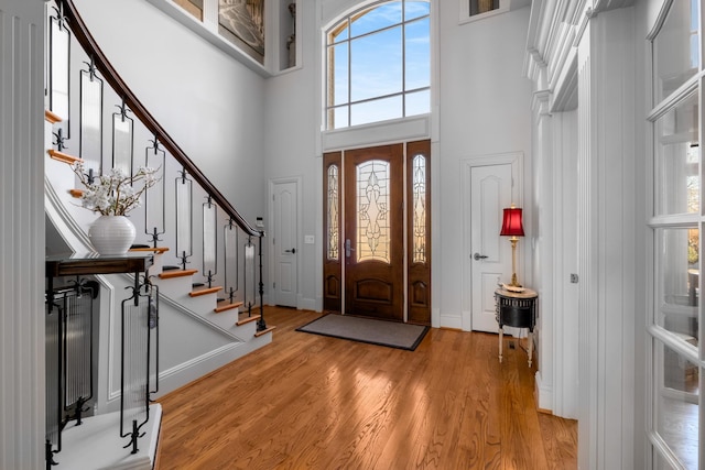 foyer entrance with baseboards, stairway, a towering ceiling, and light wood-style floors