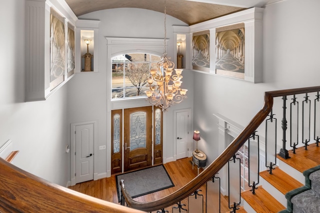 foyer entrance with baseboards, wood finished floors, stairs, vaulted ceiling, and a chandelier