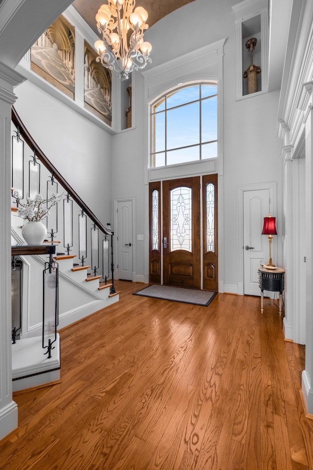 foyer with light wood finished floors, stairs, a chandelier, and ornate columns