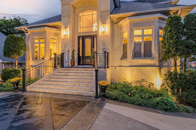 entrance to property with brick siding and a shingled roof