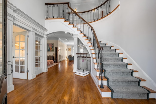 entryway featuring arched walkways, wood finished floors, a high ceiling, stairs, and crown molding