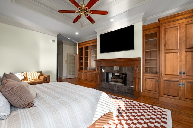 bedroom featuring ceiling fan, recessed lighting, dark wood-type flooring, a tiled fireplace, and crown molding