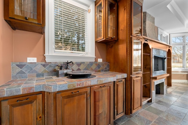 kitchen with stone tile flooring, a sink, glass insert cabinets, and brown cabinets