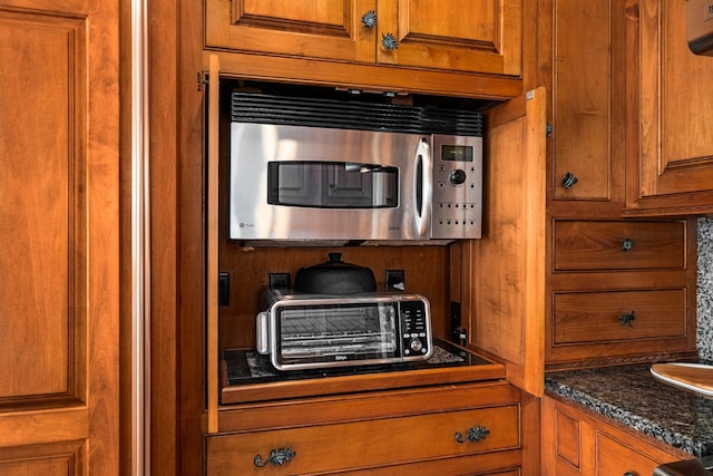 kitchen with a toaster, stainless steel microwave, dark stone countertops, and brown cabinets