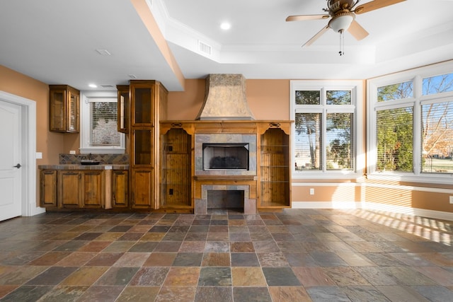 unfurnished living room featuring a ceiling fan, a tray ceiling, baseboards, and stone tile floors