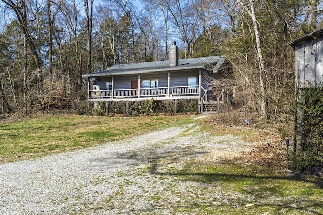 view of front of home featuring a chimney, a porch, a front yard, metal roof, and driveway