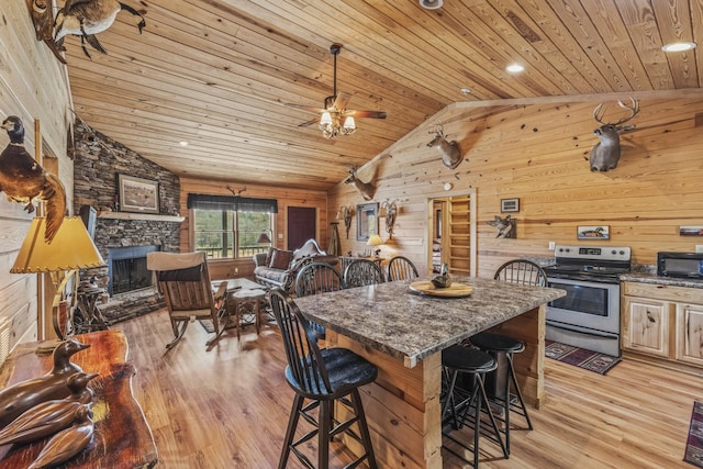 kitchen featuring wooden ceiling, stainless steel range with electric cooktop, a stone fireplace, black microwave, and a kitchen bar