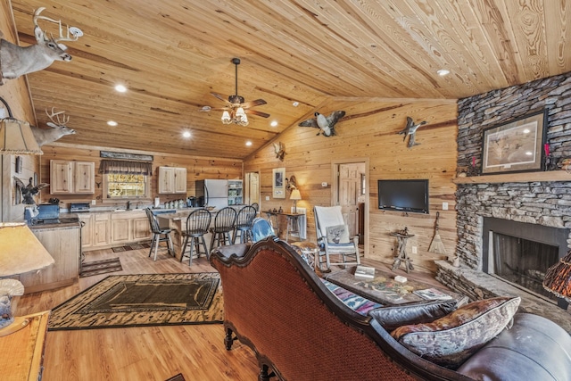 living room with wooden walls, wood ceiling, light wood-style flooring, vaulted ceiling, and a stone fireplace