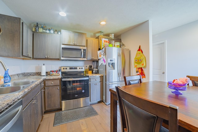 kitchen with recessed lighting, light countertops, light wood-style flooring, appliances with stainless steel finishes, and a sink