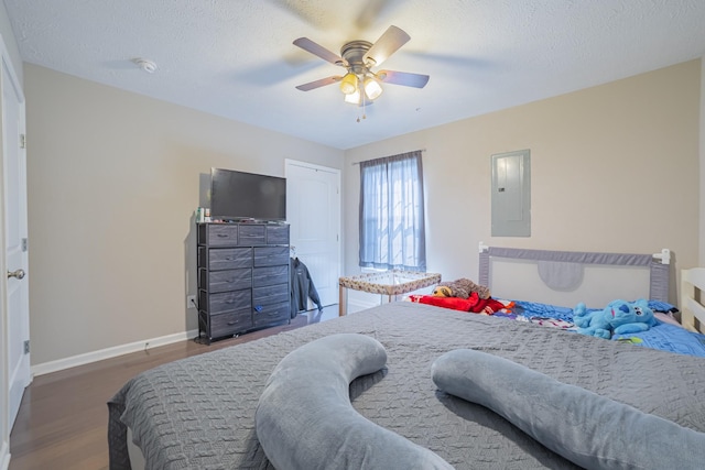 bedroom featuring electric panel, baseboards, a ceiling fan, dark wood-type flooring, and a textured ceiling