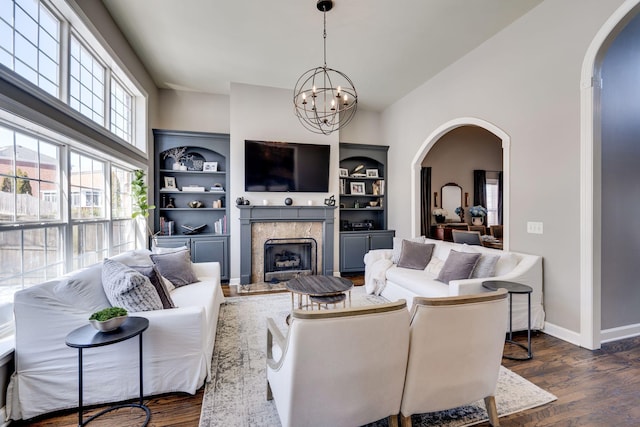 living area featuring dark wood-type flooring, arched walkways, a notable chandelier, and a premium fireplace