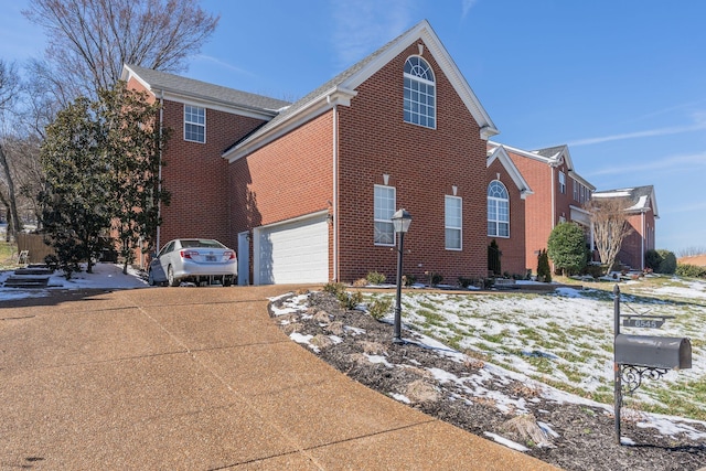 snow covered property with driveway, a garage, and brick siding