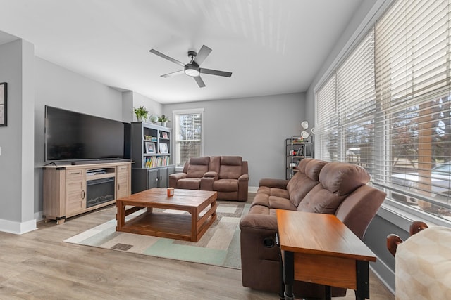 living room with light wood-type flooring, a ceiling fan, and baseboards