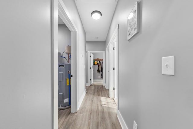 corridor with water heater, light wood-type flooring, and baseboards