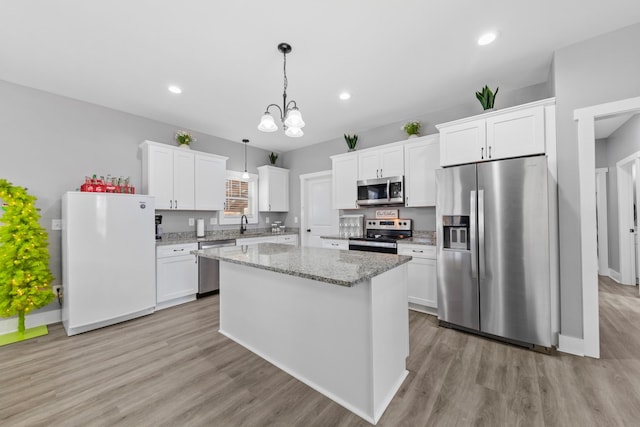 kitchen with appliances with stainless steel finishes, decorative light fixtures, a center island, light stone countertops, and white cabinetry