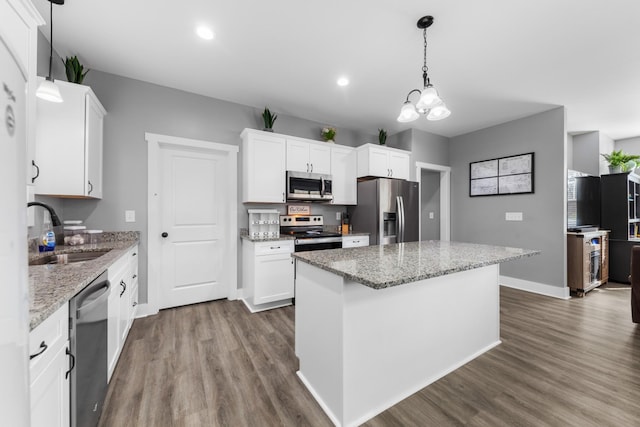 kitchen with stainless steel appliances, white cabinetry, a sink, and decorative light fixtures