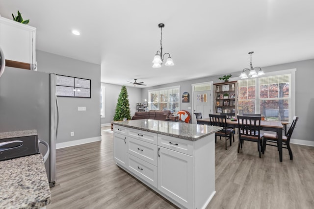 kitchen with open floor plan, hanging light fixtures, light stone countertops, and white cabinets