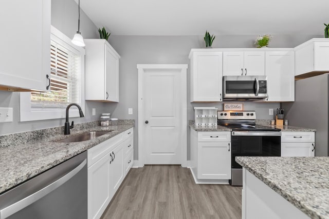 kitchen with light wood-style flooring, a sink, white cabinetry, hanging light fixtures, and appliances with stainless steel finishes