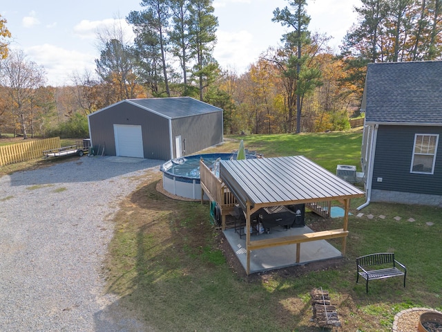 view of yard with central AC unit, a covered pool, a detached garage, an outbuilding, and gravel driveway