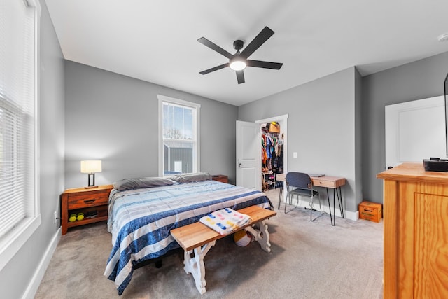 bedroom with a ceiling fan, light carpet, a spacious closet, and baseboards