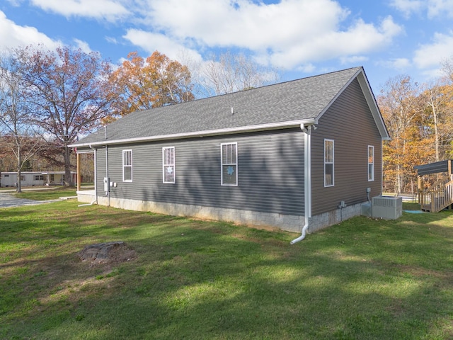 view of side of property featuring a shingled roof, cooling unit, and a yard