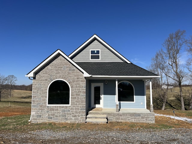 view of front of house featuring stone siding, a shingled roof, and a porch