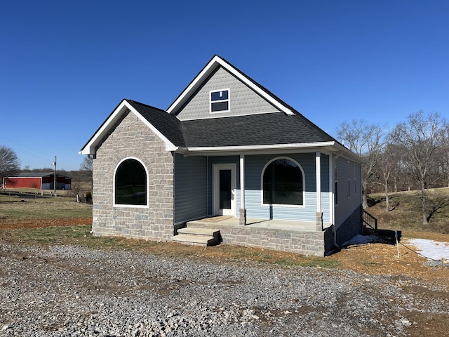 view of front facade featuring covered porch, stone siding, and roof with shingles